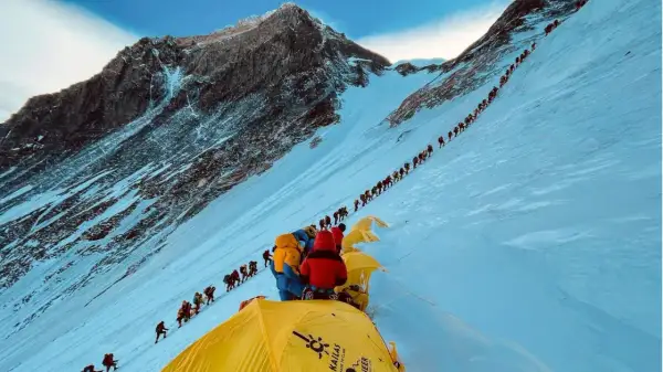 Eine lange Schlange von Bergsteigern kämpft sich den schneebedeckten Hang des Mount Everest hinauf. Die Frage, wie lange dauert es den Mount Everest zu besteigen, wird hier durch die schiere Anzahl der Menschen beantwortet.
