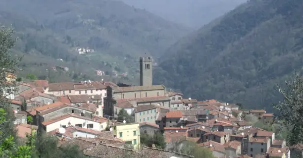 Panoramica di una villa con una basilica imponente, incastonata tra dolci colline boscose.