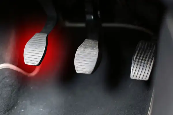 Pédales de voiture, dont l'embrayage dur est mis en évidence par une lueur rouge.