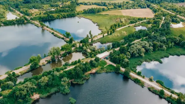Malowniczy krajobraz z licznymi stawami i dołami, otoczony zielenią. W oddali widać pola i lasy.