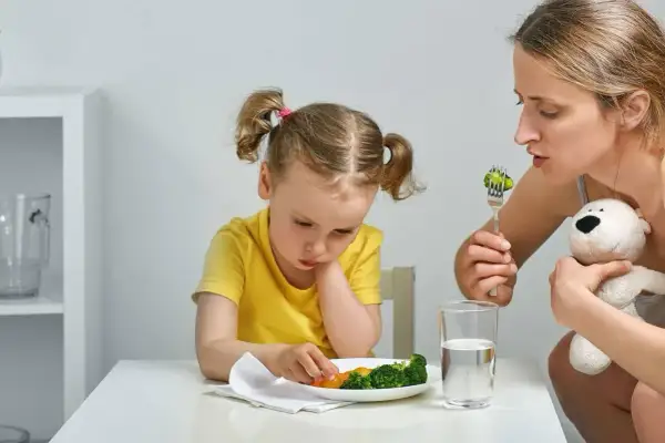 Mama zachęca dziecko do jedzenia brokułów. Trudna dieta dwulatka, ale mama się nie poddaje.