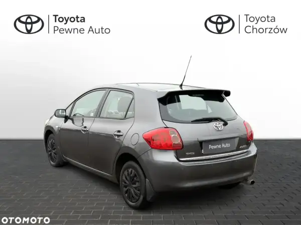 Szary Toyota Auris 2006 z przyciemnianymi szybami i spojlerem, zaparkowany na kostce brukowej.