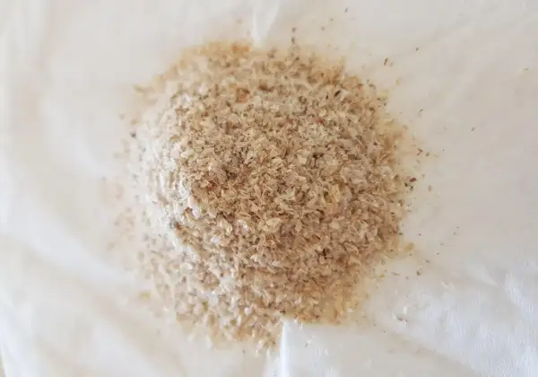 En hög med ljusbrunt fiberhusk, som ser ut som små, tunna flingor, ligger på en vit yta.
