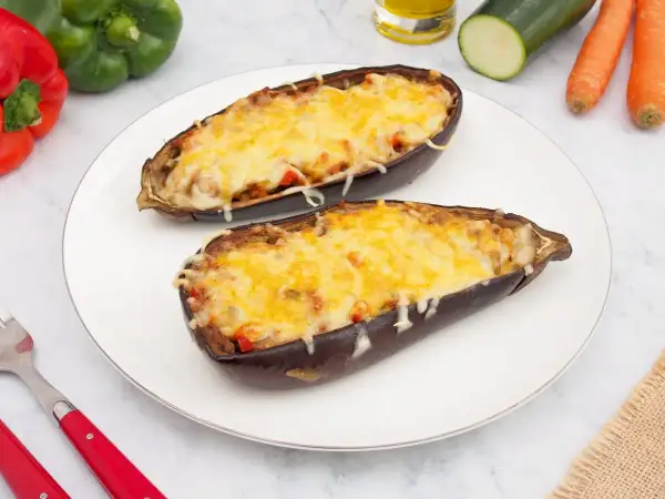 Dos mitades de berenjenas rellenas de verduras y cubiertas de queso gratinado, listas para disfrutar.