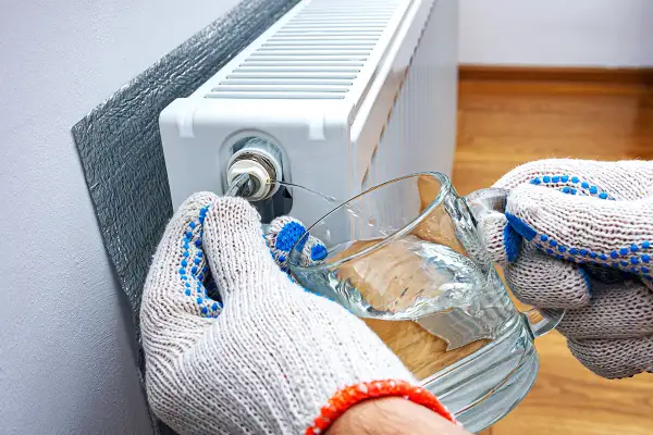 Mani guantate raccolgono acqua da un bicchiere mentre si impara come sfiatare i termosifoni, liberando l'aria intrappolata.