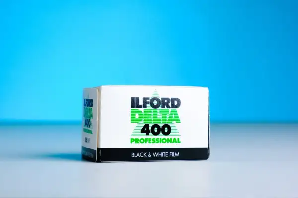A box of Ilford Delta 400 Professional black and white film sits on a white surface against a bright blue background.