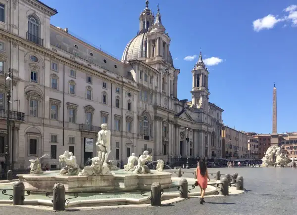 Una donna passeggia nella splendida Piazza Navona, ammirando la Fontana dei Quattro Fiumi e la maestosa chiesa.