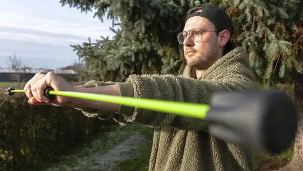 Mann mit Brille und Kappe trainiert mit einem leuchtend grünen Schwingstab, bereit für den Decathlon.