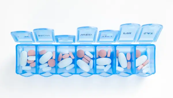 En blå medicindosa fylld med vita och rosa piller. Kan symbolisera hantering av mediciner och potentiella nackdelar med betablockerare.