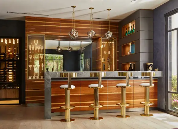 Luxurious home bar ideas featuring a marble countertop, wood cabinetry, gold bar stools, and a wine display.