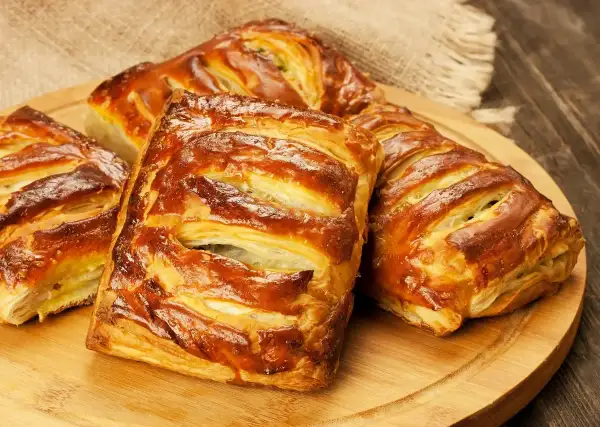 Złociste, pieczone ciasto francuskie z nadzieniem, ułożone na drewnianej desce.