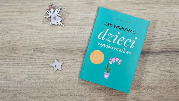 Książka "Jak wspierać dzieci wysoko wrażliwe" na drewnianym tle, obok aniołka i gwiazdki.