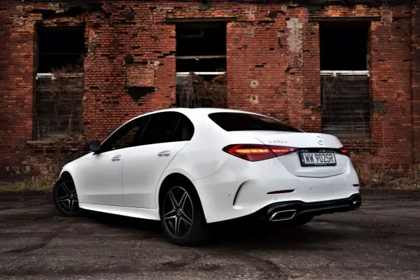 Biały Mercedes C 220 d z czarnymi felgami na tle zrujnowanej ceglanej ściany.