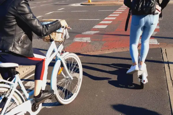 Osoba na rowerze i osoba na hulajnodze elektrycznej jadą po ścieżce rowerowej.