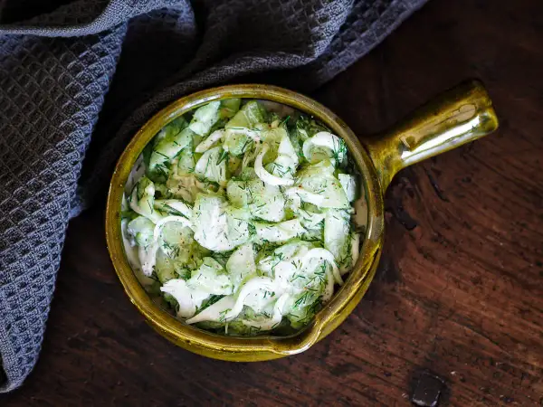 Salade de concombre à la crème, garnie d'aneth frais, servie dans un bol en céramique jaune sur une table en bois rustique.