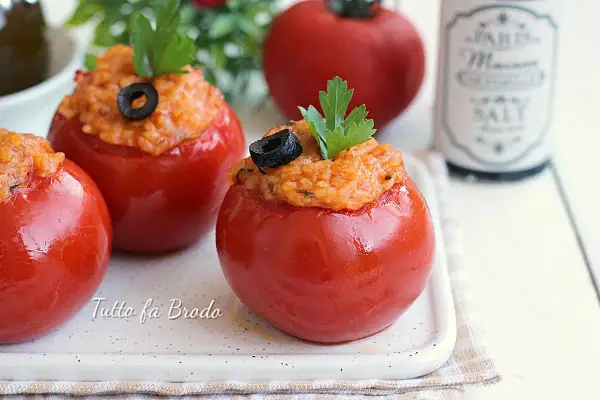 Pomodori ripieni di riso, guarniti con olive nere e prezzemolo, su un piatto bianco.