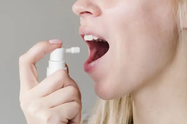 Persona aplica spray bucal con gluconato de clorhexidina para aliviar el dolor de garganta.