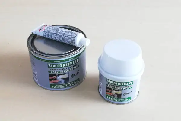 Due barattoli di stucco metallico, uno aperto con un tubetto di indurente sopra. Pronto per riparare metalli.