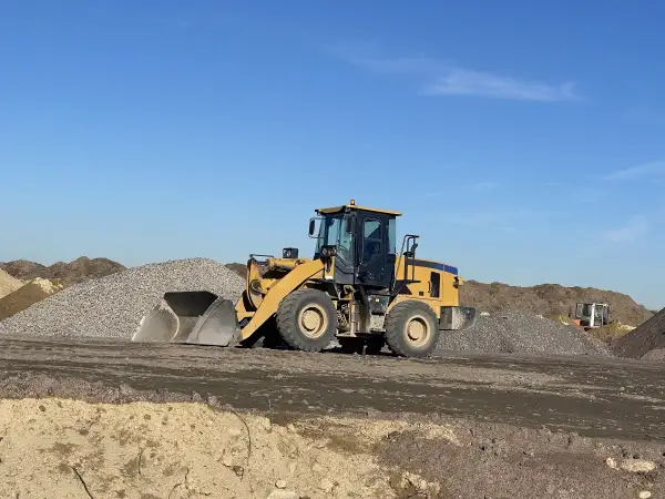 Chargeuse jaune en action pour décaissement de terrain, entourée de tas de gravats et de terre sous un ciel bleu clair.