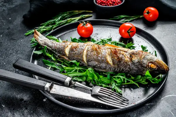 Un bar au four, doré et savoureux, servi sur un lit de roquette avec des tomates cerises et des herbes. Un plat simple et élégant.