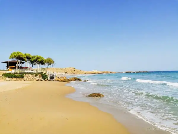 Piękne zakynthos plaże z piaszczystym brzegiem, turkusową wodą i kamienistymi wysepkami. W oddali widać biały domek i zielone drzewa.
