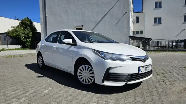 Biała Toyota Corolla 2017 zaparkowana na placu przed budynkiem.