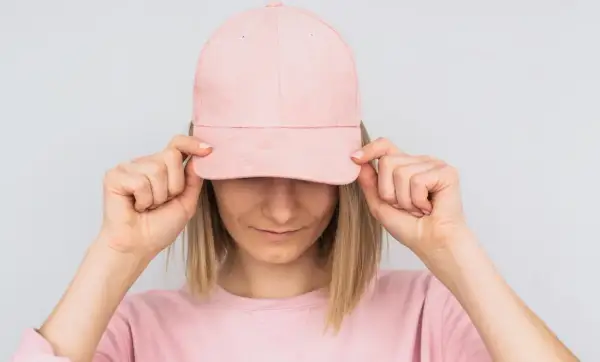 Frau mit rosa Cap, die sie mit beiden Händen vor die Augen hält. Sie zeigt, wie man eine Cap richtig tragen kann.