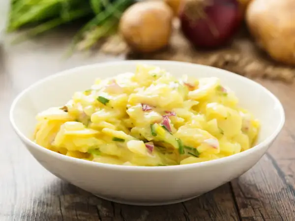 Omas Kartoffelsalat in einer Schüssel, mit Zwiebeln und Schnittlauch, auf einem Holztisch.
