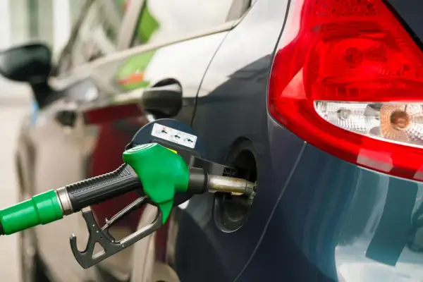 Grön bensinpump fyller på en mörkblå bil. Tänk på din bensin per km för att köra smartare.