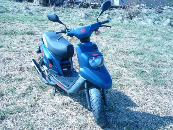 Niebieski skuter Yamaha MBK z czerwonymi akcentami stoi na trawiastym podwórku.