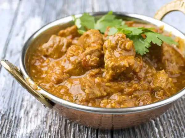 Un savoureux colombo d'agneau, mijoté dans une sauce épicée et garni de coriandre fraîche, servi dans un bol en cuivre.