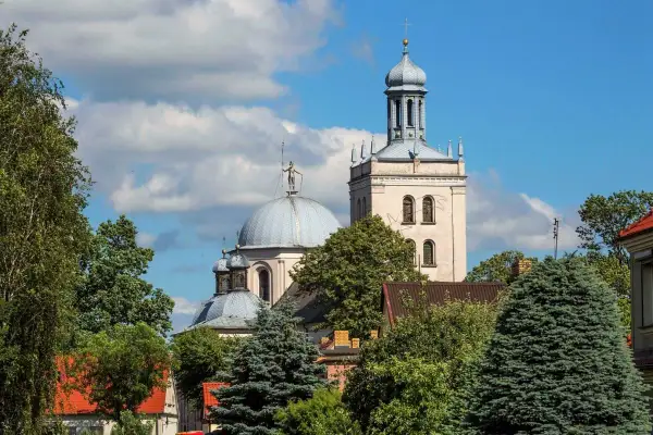 Majestatyczna fara w Grodzisku Wlkp. z kopułą i wieżą, otoczona zielenią drzew.