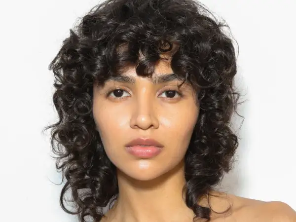 Volto di donna con capelli ricci scuri e un audace taglio capelli anni 80 mullet.