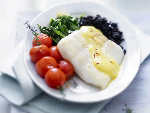 Filet de poisson blanc nappé de sauce safranée, accompagné de tomates cerises rôties, d'épinards et de riz noir. Une belle recette de turbot.