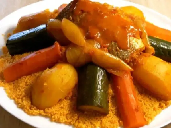 Un plat généreux de couscous garni de poisson, carottes, courgettes et pommes de terre, le tout nappé d'une sauce savoureuse.