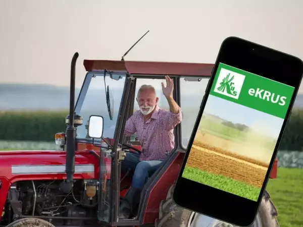 Uśmiechnięty rolnik w traktorze macha do kamery, obok smartfon z aplikacją eKRUS, która ułatwia zarządzanie prawem do emerytury rolniczej według nowych zasad.
