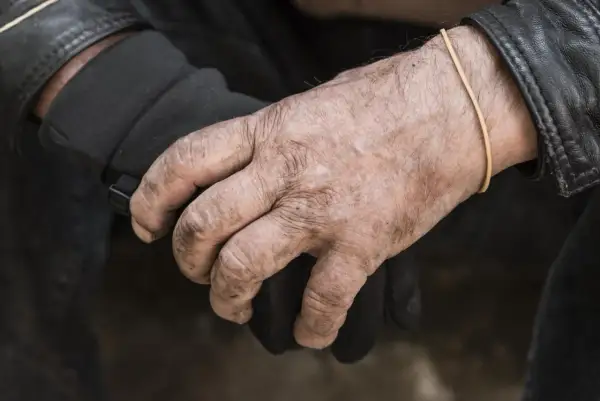 Manos secas y curtidas, con una goma elástica en la muñeca, sujetan un guante negro.