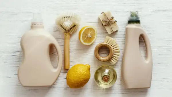 Dos botellas de detergente, jabón, limones y cepillos de madera para una limpieza sostenible.