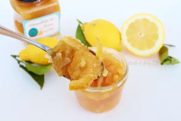 Un cucchiaio raccoglie la marmellata di limoni fatta in casa, con limoni freschi e foglie sullo sfondo.