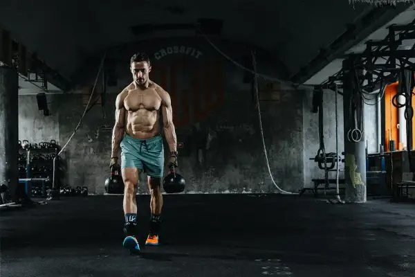 Mężczyzna z imponującą muskulaturą idzie z odważnikami w siłowni. To dowód, że crossfit dla kogo? Dla każdego, kto chce budować siłę i wytrzymałość!