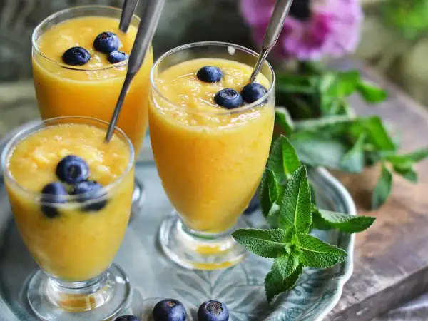 Tre glas med krämig mango smoothie, toppade med blåbär och mynta. En perfekt, uppfriskande dryck.