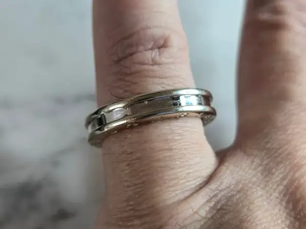 Anillo Bulgari de oro blanco y detalles pulidos, adornando un dedo con su diseño elegante y atemporal.