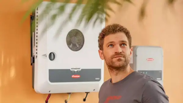 Hombre mirando hacia arriba junto a un inversor Fronius GEN24, símbolo de energía solar eficiente y sostenible.