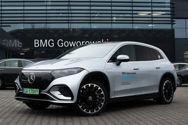 Srebrny Mercedes EQS SUV z napisem "BMG Goworowski EQS SUV jazda testowa" przed salonem samochodowym.