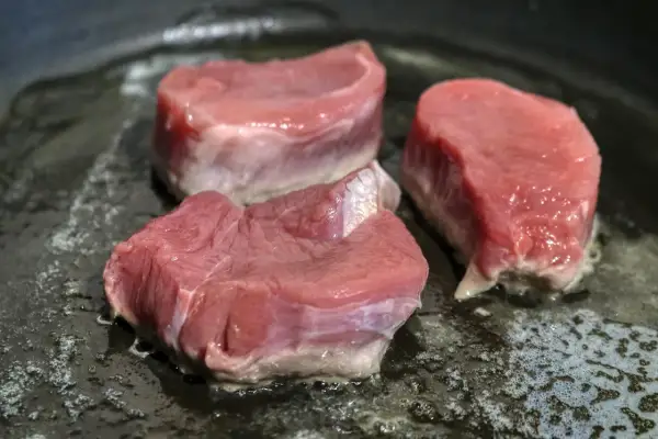 Drei saftige Schweinefilet-Medaillons braten in einer heißen Pfanne. Perfekt für köstliche Schweinefilet Rezepte.