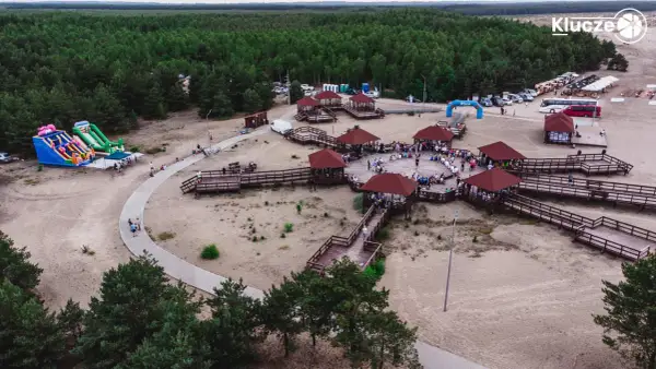 Drewniane zadaszone altany i ścieżki na piaszczystym terenie w miejscowości Klucze, otoczone lasem.