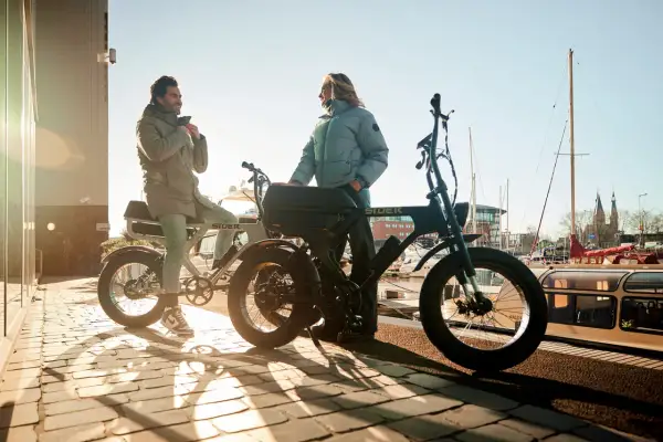 Twee mensen bij hun fatbikes aan het water. De vraag "hoe zwaar is een fatbike" komt op, maar deze stoere e-bikes lijken verrassend licht.