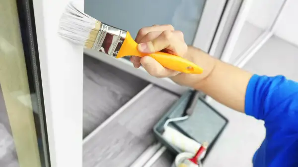 Hand streicht mit Pinsel weiße Farbe auf Kunststoffrahmen. Wetterfestes Ergebnis für Fenster und Türen.