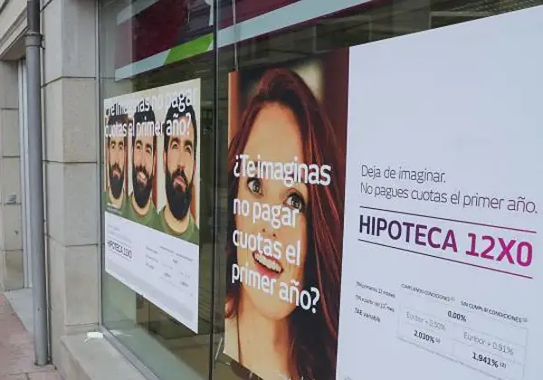 Anuncios de hipotecas en un escaparate. Uno muestra tres hombres y pregunta "¿Te imaginas no pagar cuotas el primer año?". Otro, con una mujer, dice "Deja de imaginar. No pagues cuotas el primer año. HIPOTECA 12X0". Se ve un **euribor forecast** en la ...
