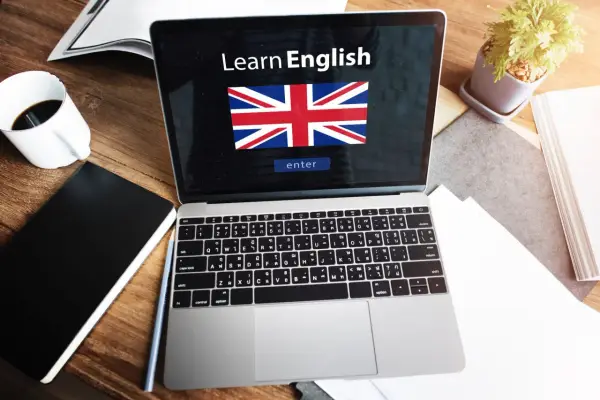 Laptop z napisem "Learn English" i flagą Wielkiej Brytanii. Obok kawa, notatnik i roślina. Idealne do nauki fce use of english.